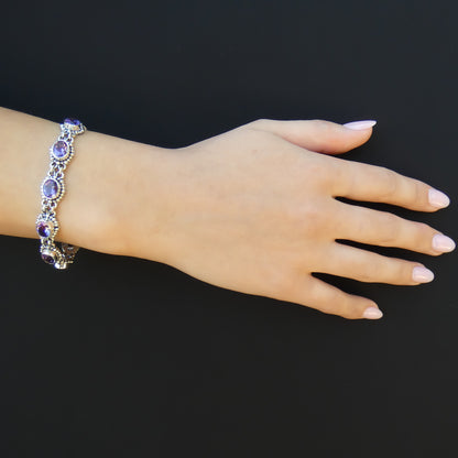 Woman wearing a silver bracelet with oval purple amethyst gemstones, and beaded accents.