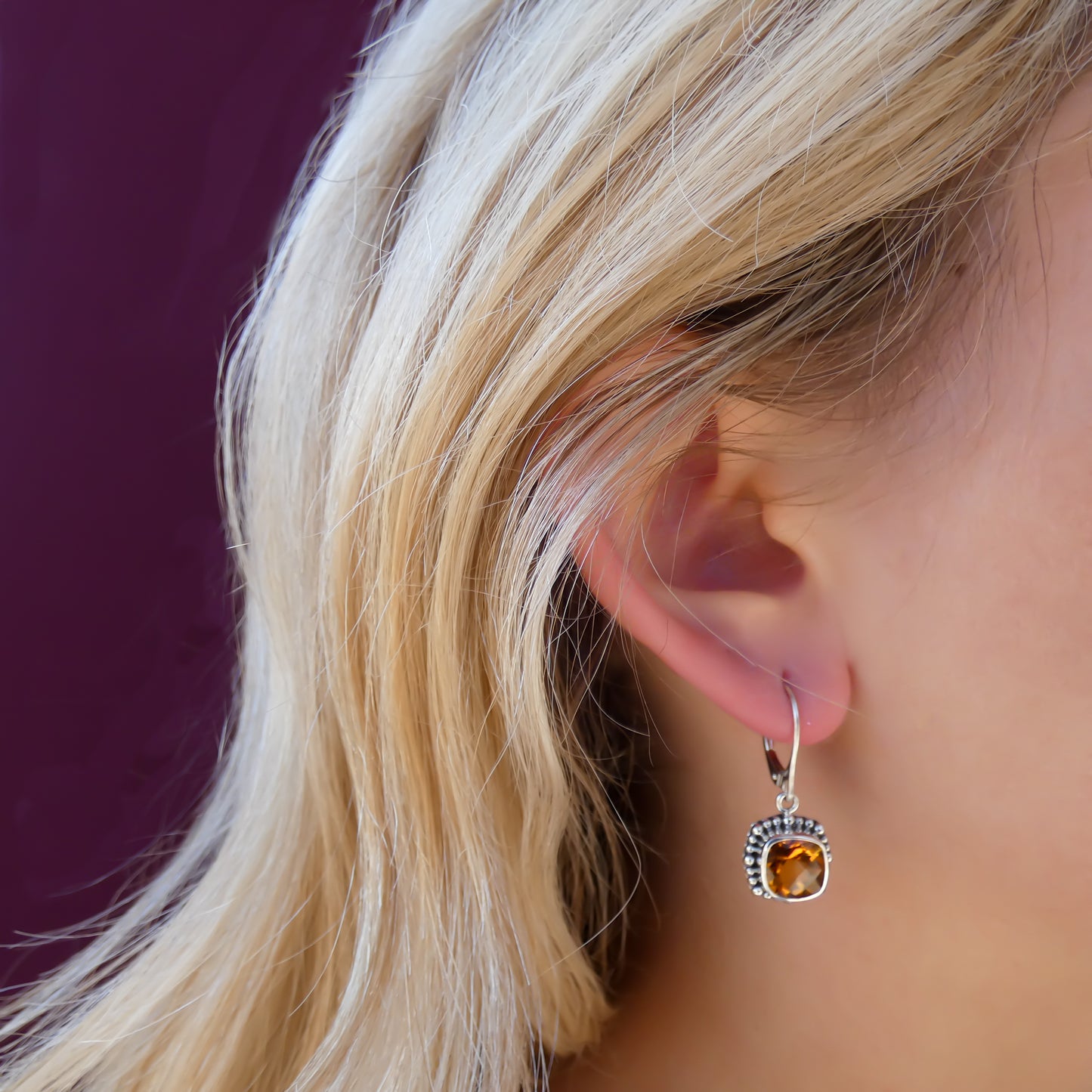 Woman wearing silver earrings with square citrine gemstones.