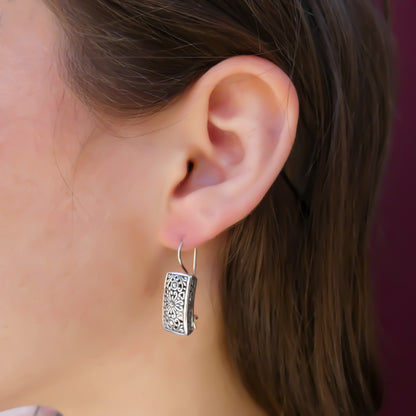 Woman wearing silver filigree rectangle earrings.