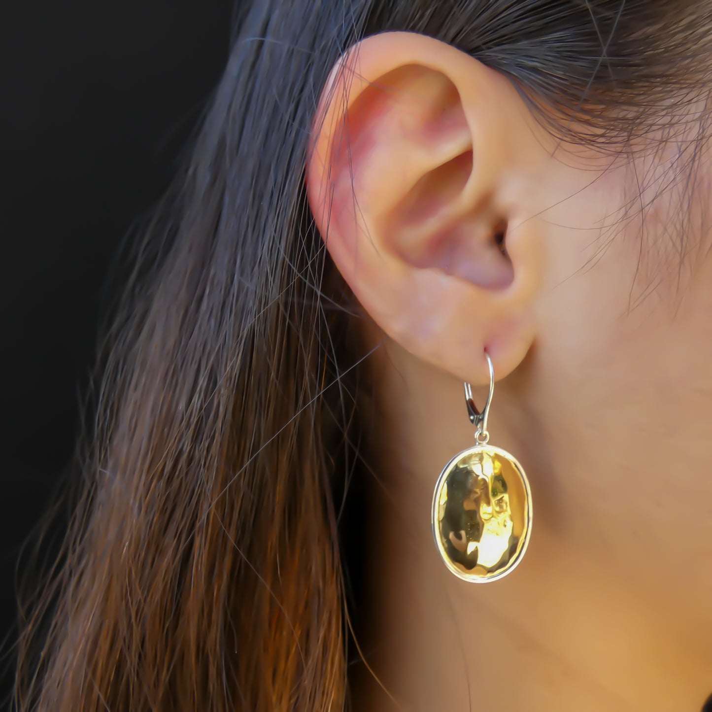 Woman wearing silver and gold oval hammered earrings.
