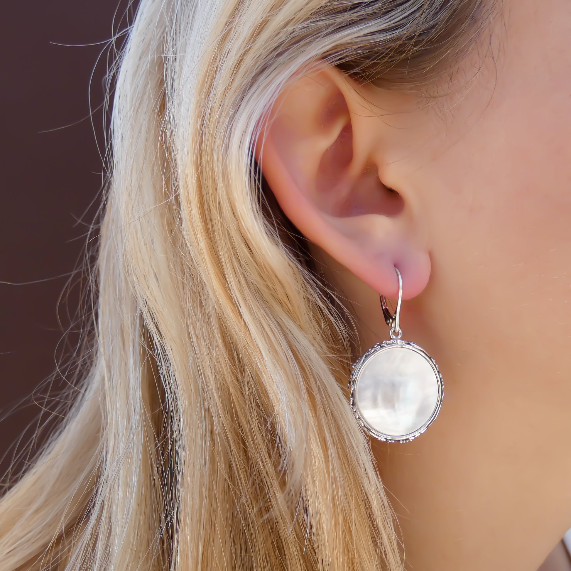 Woman wearing silver filigree and bead earrings with round mother of pearl discs.