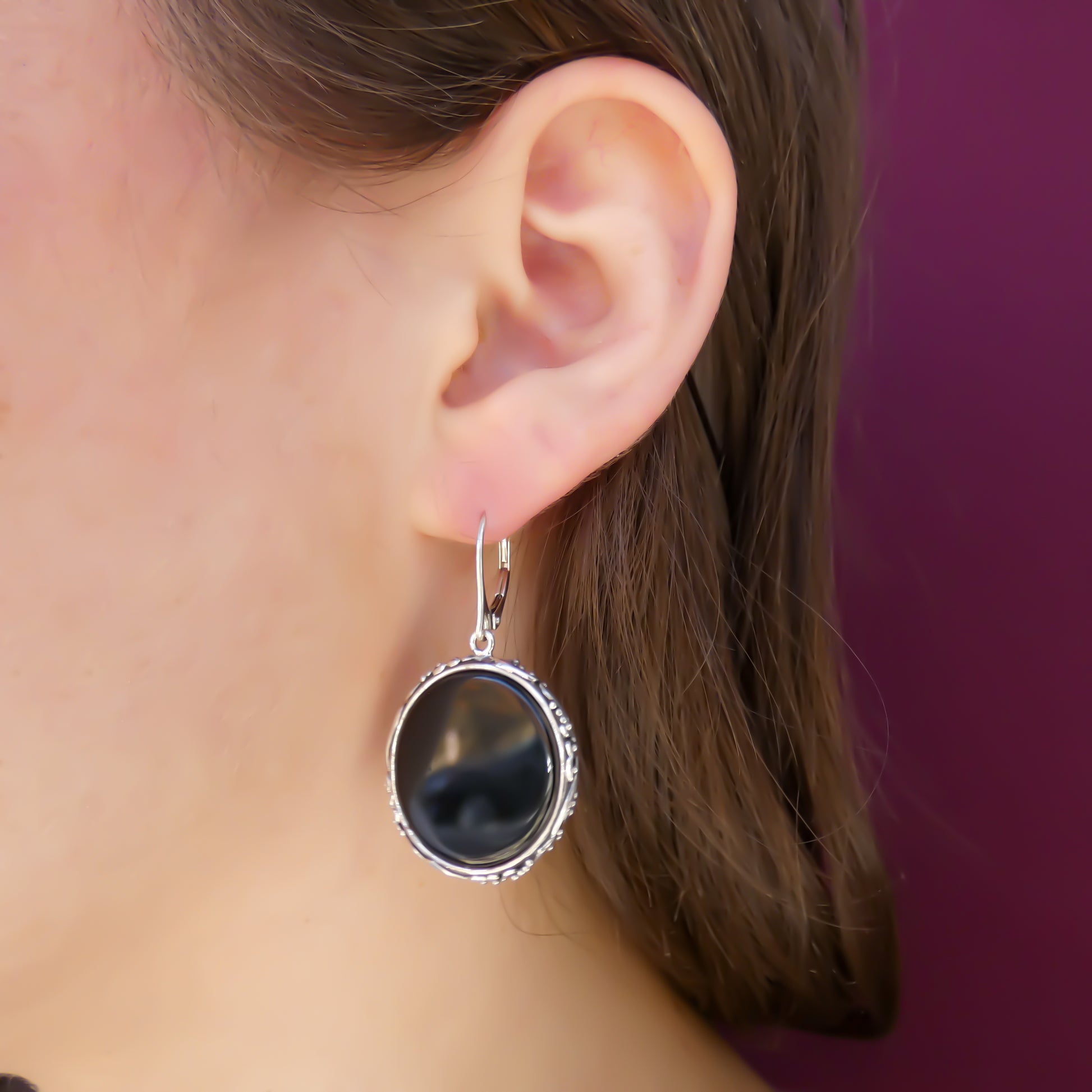 Woman wearing silver filigree and bead earrings with round onyx discs.