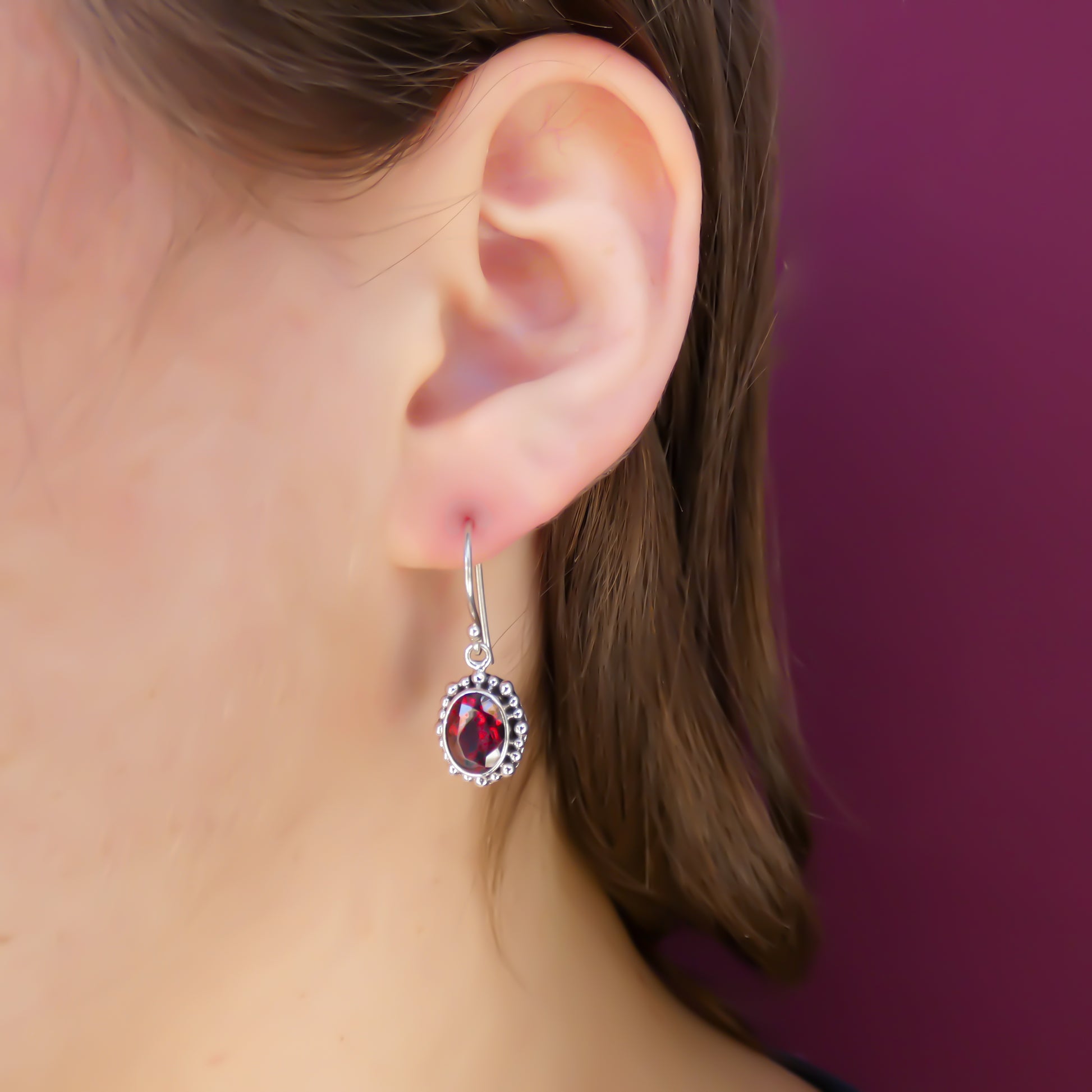Woman wearing silver earrings with faceted garnet gemstones.