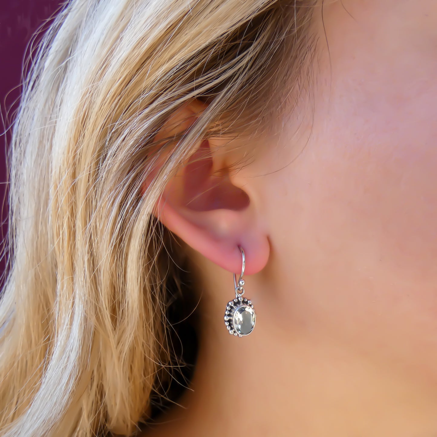 Woman wearing silver earrings with oval green amethyst gemstones.