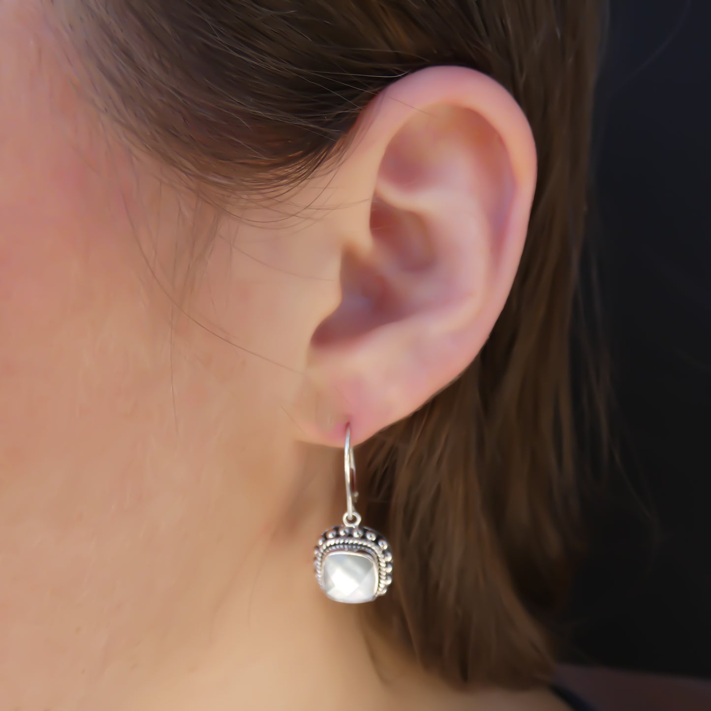 Woman wearing silver earrings with square mother of pearl doublet gemstones.