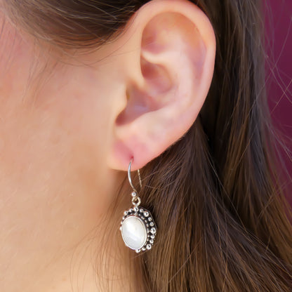 Woman wearing silver earrings with oval mother of pearl stones.