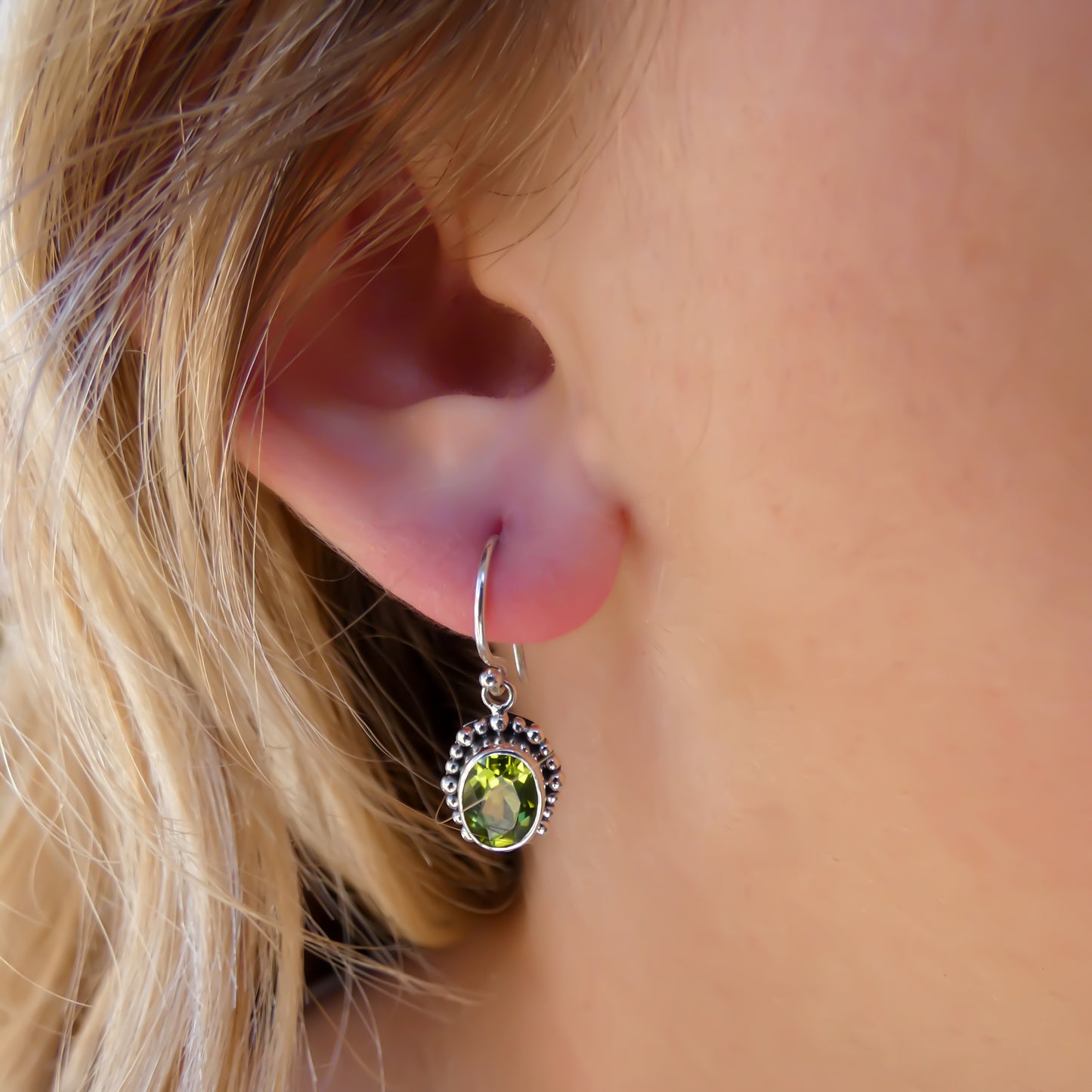 Woman wearing silver earrings with oval peridot gemstones.