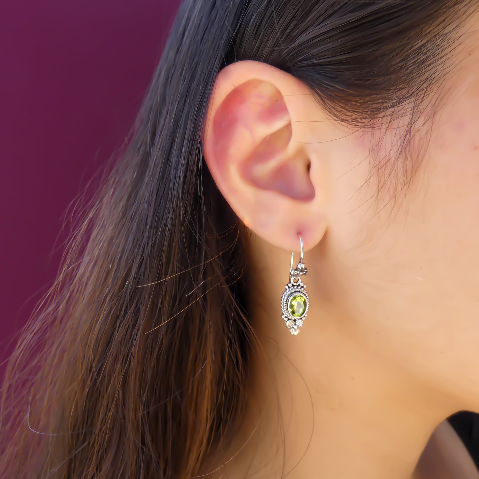 Woman wearing silver wire earrings with floral design and peridot stones.