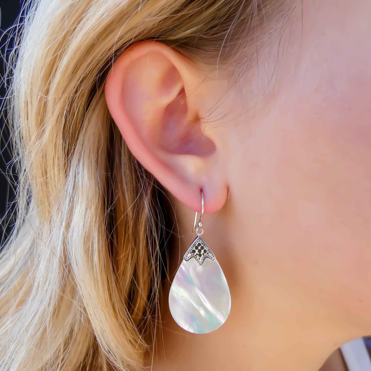 Woman wearing silver earrings with shell drop stones.