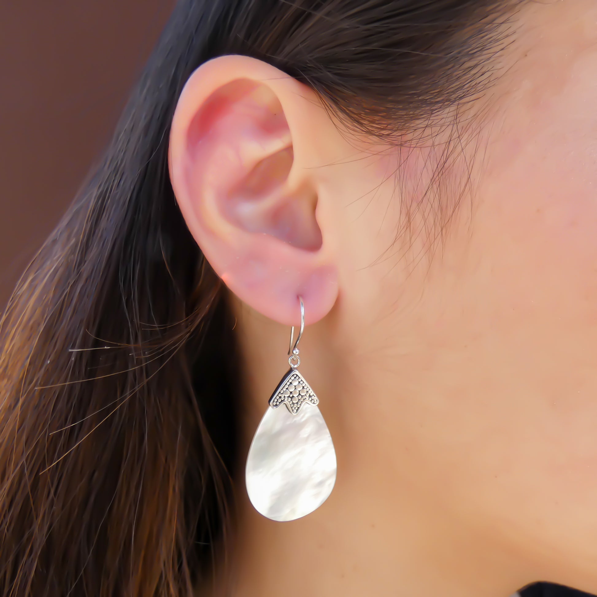 Woman wearing silver earrings with teardrop shell.